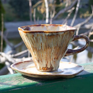 May include: A ceramic teacup and saucer set with a unique, textured, wood-grain design in shades of brown, beige, and white.