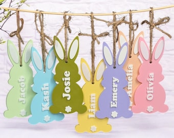Op de afbeelding: Zeven pastelkleurige houten bunny-versieringen met namen erop geschreven. De namen zijn Jacob, Kash, Josie, Liam, Emery, Amelia en Olivia.