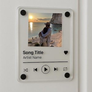 Puede incluir: Placa de acrílico transparente con una foto de una pareja abrazándose en una playa al atardecer. La placa presenta un diseño de interfaz de reproductor de música con campos de texto para "Song Title" y "Artist Name", junto con iconos de reproducción, salto y repetición. Fijaciones circulares negras.