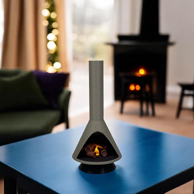 May include: A gray tabletop fireplace with a faux fire inside. The fireplace is on a blue table with a blurred background.