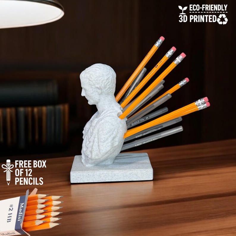 Julius Caesar bust pen holder 3D printed in marble effect PLA, shown with pencils inserted in the back, placed on a classic wooden desk. Includes a free box of 12 pencils, perfect for history lovers, teachers, and unique office decor enthusiasts. Handmade eco-friendly sculpture, ideal as a conversation starter and a clever blend of humor and functionality for home or office workspaces.
