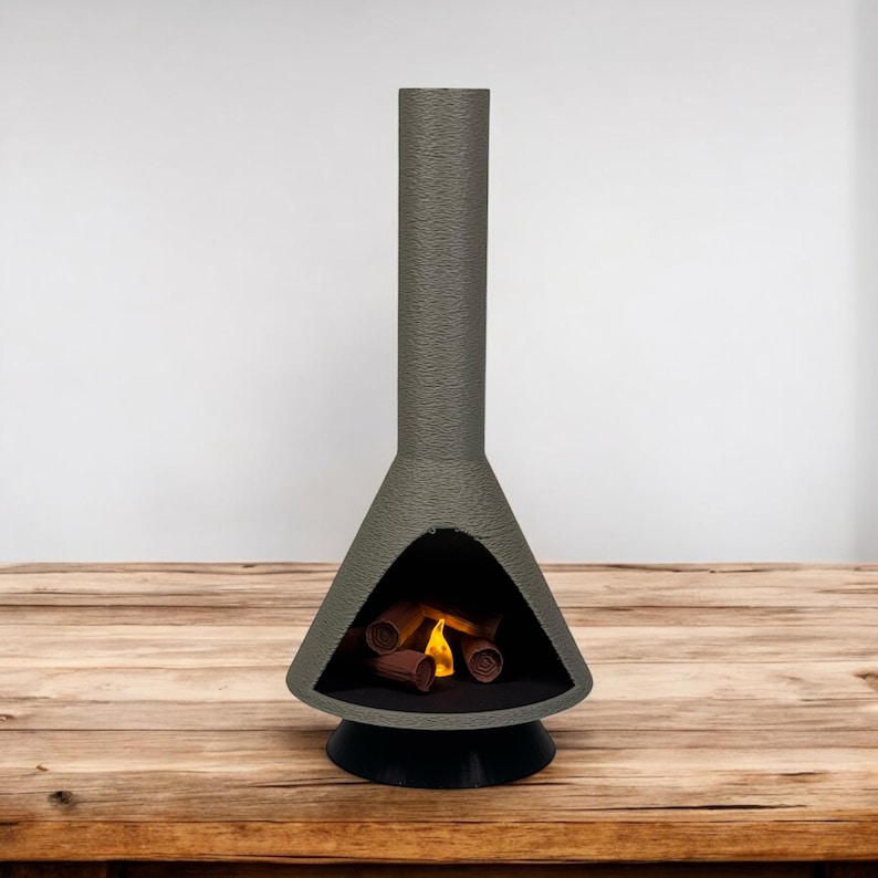 May include: A gray concrete fireplace with a black base and a chimney. The fireplace has a fire burning inside with logs and flames.