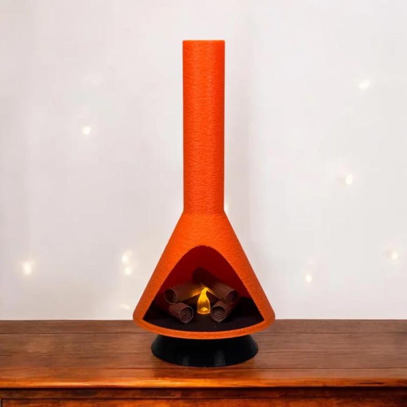 May include: A bright orange ceramic fireplace with a black base and a faux fire inside. The fireplace is shaped like a cone with a tall chimney.