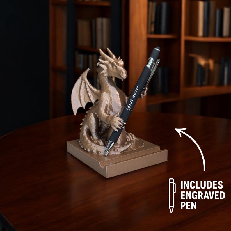 Puede incluir: Un portal&aacute;pices de drag&oacute;n de color bronce con un bol&iacute;grafo grabado. El drag&oacute;n est&aacute; posado sobre una base rectangular, sosteniendo el bol&iacute;grafo. El bol&iacute;grafo es negro con detalles plateados y tiene la inscripci&oacute;n "Your name".