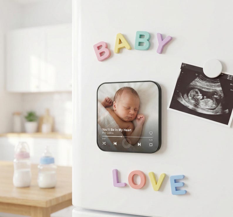 May include: A white refrigerator door displays colorful magnetic letters spelling "BABY" and "LOVE". A photo of a sleeping infant is on a black square magnet. An ultrasound image is also attached with a round magnet. Baby-themed decor.