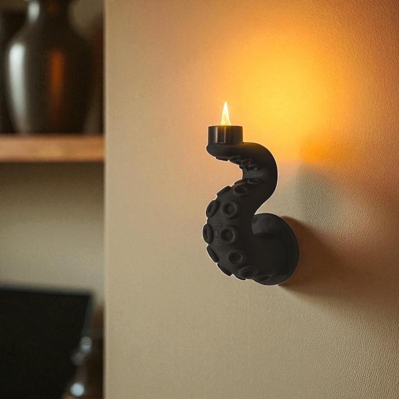 May include: A black octopus tentacle wall sconce with a small candle. The tentacle is detailed with suction cups and curves upwards, holding the candle. The candle flame glows against the wall.