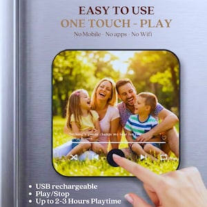 May include: A rectangular, black and silver device with rounded corners, featuring a family photo on the screen. The device has the text "EASY TO USE" and "ONE TOUCH - PLAY". Additional text includes "USB rechargeable", "Play/Stop", and "Up to 2-3 Hours Playtime".