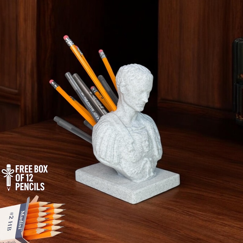Julius Caesar bust pen holder 3D printed in marble effect PLA, shown with pencils inserted in the back, placed on a classic wooden desk. Includes a free box of 12 pencils, perfect for history lovers, teachers, and unique office decor enthusiasts. Handmade eco-friendly sculpture, ideal as a conversation starter and a clever blend of humor and functionality for home or office workspaces.