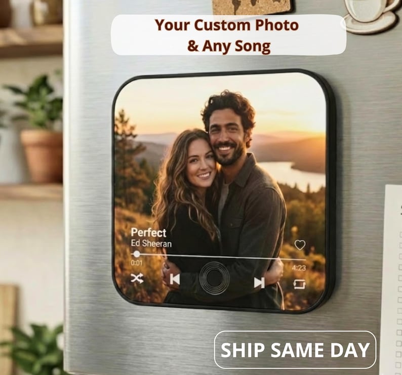 Square personalized music box magnet on a stainless steel refrigerator, displaying a couple’s photo with a Spotify-style music player overlay (song title and controls). Text reads ‘Your Custom Photo & Any Song’ and ‘SHIP SAME DAY’ — custom photo song magnet gift.