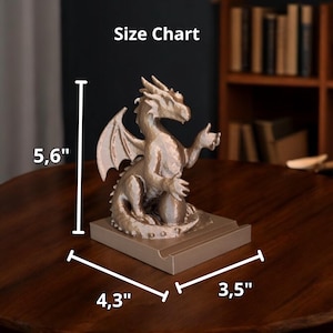 Puede incluir: Una figura de drag&oacute;n dorada met&aacute;lica, de 14,2 cm de alto, 10,9 cm de ancho y 8,9 cm de profundidad. El drag&oacute;n est&aacute; sentado sobre una base rectangular, con las alas extendidas y un brazo levantado. El texto "Size Chart" es visible.