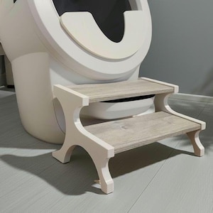 May include: A two-step wooden stool with a light wood grain finish on the steps and white supports. The stool is designed to assist with reaching a toilet, with a white toilet in the background.