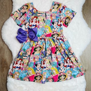 May include: A colourful princess-themed dress with short sleeves and a round neckline. The dress features a print of various Disney princesses, including Snow White, Cinderella, and Ariel. The dress is made of a soft and comfortable fabric.