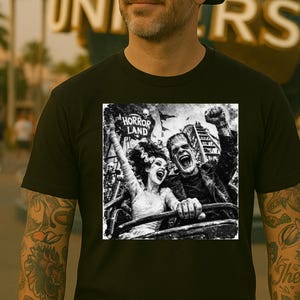 May include: Black t-shirt featuring a black and white graphic of Frankenstein and his bride on a roller coaster, with the text "HORROR LAND". The image captures a moment of excitement and fear.