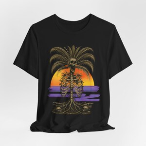 May include: A black short-sleeve t-shirt featuring a graphic print of a palm tree with a human ribcage as its trunk and a skull at the top. The design includes a sunset background with orange and yellow hues, purple horizontal lines, and roots.