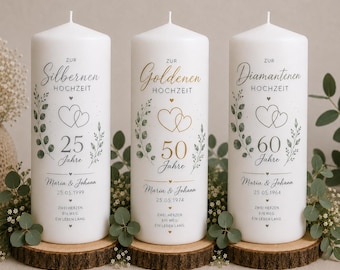 Könnte beinhalten: Drei weiße zylindrische Stumpenkerzen mit aufgedrucktem Text und botanischen Illustrationen. Die Kerzen sind für die silberne, goldene und diamantene Hochzeit beschriftet, mit den Namen Maria & Johann, Daten und dem Spruch Zwei Herzen, Ein Weg, Ein Leben lang.