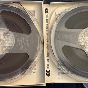 May include: Two vintage magnetic tape reels in their original boxes. The reels are clear plastic with dark tape inside. One reel has the text "Magnetic Tape" and the other has "Side 1". The boxes have printed text and arrows.