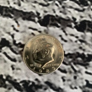 May include: A silver US half dollar coin with the profile of John F. Kennedy on the obverse. The coin reads "Liberty" and "In God We Trust" and is dated 1983.