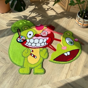 Könnte beinhalten: Ein grüner und roter Cartoon-Teppich mit zwei Figuren aus der Happy Tree Friends-Zeichentrickserie. Die Figuren sind ein Eichhörnchen und eine grüne Kreatur mit einem großen Maul. Der Teppich ist aus Plüsch gefertigt und hat ein verspieltes Design.
