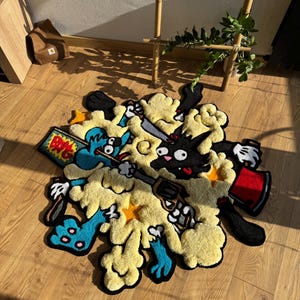 Könnte beinhalten: Ein bunter Cartoon-Teppich mit einer blauen und schwarzen Figur, die eine Pistole und einen roten Eimer hält. Der Teppich ist aus flauschigem Garn gefertigt und hat einen gelben Hintergrund mit schwarzen Umrissen.
