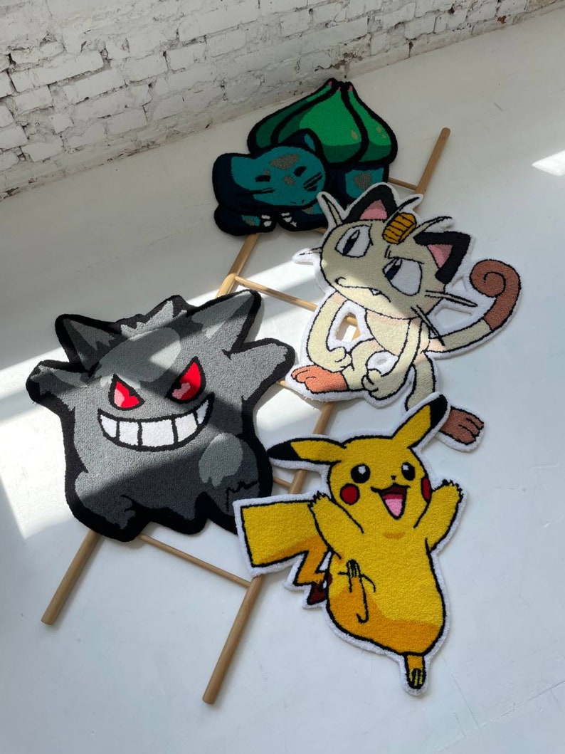 May include: Four colorful, cartoon character rugs. A gray Gengar rug with red eyes and a wide smile. A yellow Pikachu rug with arms raised. A Meowth rug with a gold coin on its head. A green and blue Bulbasaur rug.