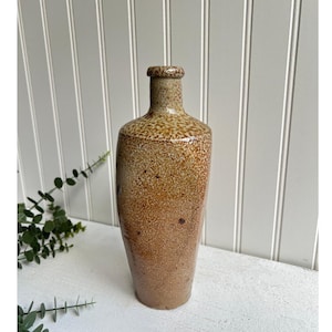 Op de afbeelding: Een keramische vaas met een gespikkeld bruin en wit glazuur. De vaas heeft een rond lichaam en een smalle hals.