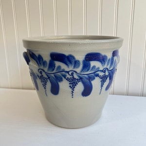 Könnte beinhalten: Ein Steingut-Pflanzgefäß mit hellgrauem Grund und einem blauen Weinranken-Design. Der Pflanztopf hat eine runde Form mit zwei kleinen Griffen und ist für den Innen- und Außenbereich geeignet.