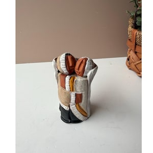 May include: A ceramic sculpture of two stylized figures embracing. The figures have tan faces and are wearing white, tan, orange, and black clothing. The sculpture is on a white surface.