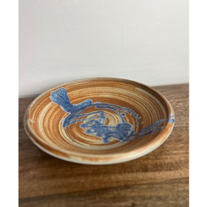 May include: A brown ceramic bowl with blue and white glaze. The bowl has a swirl pattern and a blue design in the center.