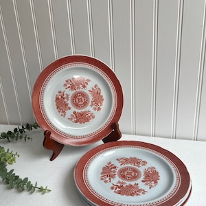 May include: Set of four white ceramic salad plates with a red floral design. The plates have a scalloped edge and a raised center design.