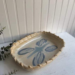 May include: A ceramic serving dish with a light brown rim and a blue and white floral design.
