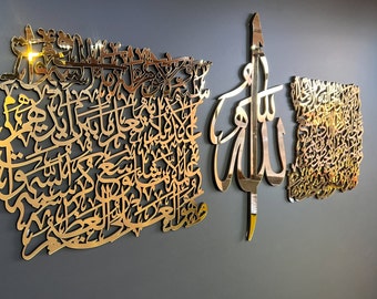 May include: Gold-colored metal wall art featuring Arabic calligraphy. The art is in the shape of a large rectangle and a smaller rectangle with the word "Allah" in the center.