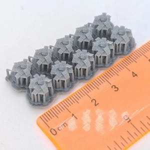 May include: A set of ten small, gray, 3D-printed resin miniature structures, each featuring a multi-faceted roof and vertical support pillars. An orange plastic ruler is positioned alongside the miniatures, showing they measure approximately 1.5 inches in total length.