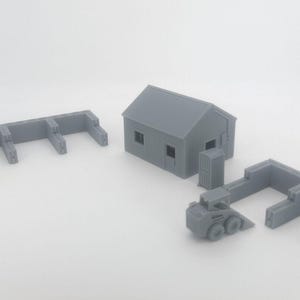 May include: Gray miniature construction set featuring a small house, a skid steer loader, and wall sections. The set is made of a solid gray material and is designed to resemble a construction site.