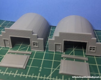 May include: Two gray, 3D printed, model kits of arched buildings with garage doors and windows. The kits are assembled and sitting on a green cutting mat. There are two additional gray, 3D printed, model kits of garage doors.