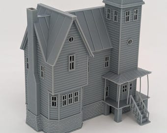 May include: A gray, unpainted 3D-printed miniature model of a two-story house featuring a tall tower, a front porch with stairs, a chimney on the side, multiple rectangular windows, and a textured brick-style foundation base.
