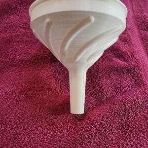 May include: A white plastic funnel with a textured, spiral design on the inside. The funnel is sitting on a pink towel.