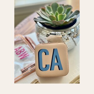 May include: A beige travel jewelry case with the initials "CA" in blue lettering.