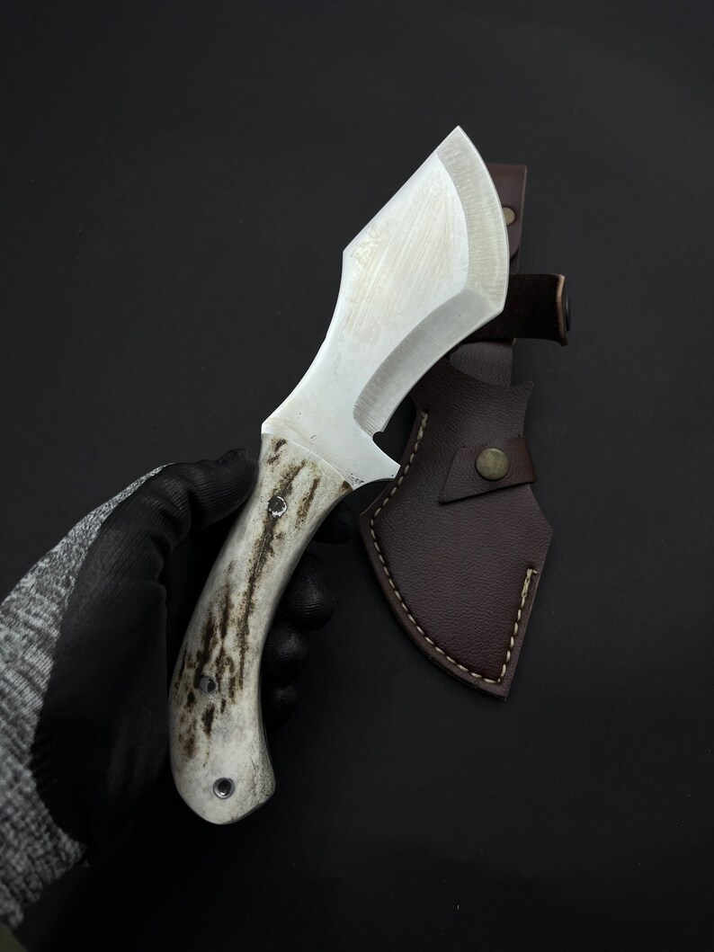 May include: A white-handled knife with a brown leather sheath. The knife has a curved blade and a textured handle.