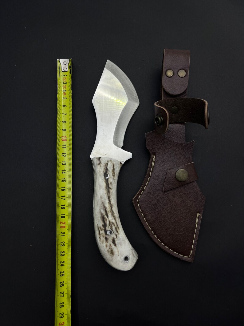 May include: A white-handled knife with a brown leather sheath. The knife has a silver blade and a white handle with a brown pattern. The sheath has a brown leather strap with a metal buckle.