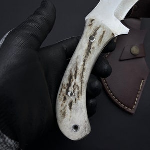 May include: A white handled knife with a brown leather sheath. The handle has a textured pattern and three metal rivets.