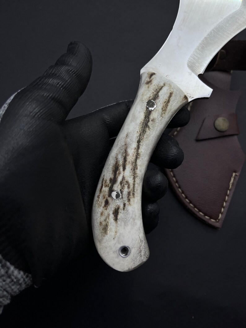 May include: A white handled knife with a brown leather sheath. The handle has a textured pattern and three metal rivets.