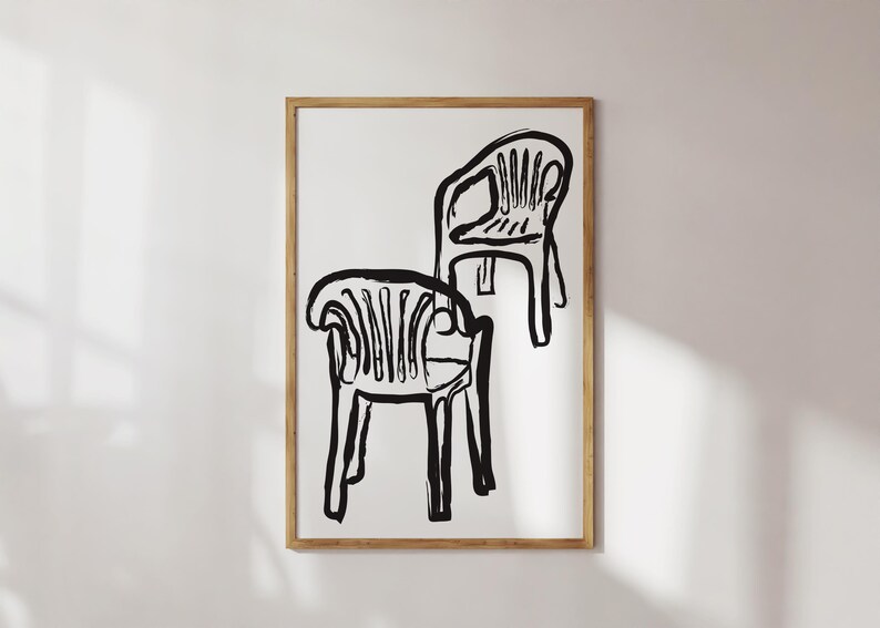 May include: Black and white art print featuring two stylized chairs. The chairs are depicted with bold, brushstroke-like lines, creating a minimalist and modern aesthetic. The artwork is framed in a natural wood frame, adding a touch of warmth.