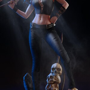 Puede incluir: Estatua detallada de una mujer con top y pantalones de corsé negros, sosteniendo un arma grande. La estatua está sobre una formación rocosa con calaveras. La mujer tiene el pelo largo y rubio y lleva una gargantilla.