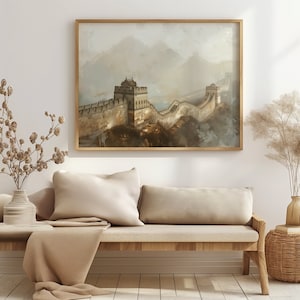May include: A framed painting of the Great Wall of China, with a misty background and a brown wooden frame. The painting is hanging on a white wall above a light brown couch with two pillows.