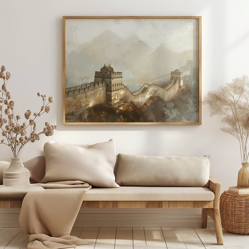 May include: A framed painting of the Great Wall of China, with a misty background and a brown wooden frame. The painting is hanging on a white wall above a light brown couch with two pillows.