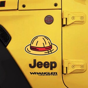 May include: A yellow straw hat sticker with a red band applied to the yellow side panel of a Jeep Wrangler Unlimited vehicle. The sticker is positioned above the black Jeep logo and the Trail Rated 4x4 badge on the metal body.