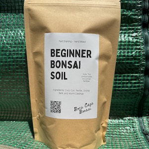May include: A tan paper bag of "BEGINNER BONSAI SOIL" with a white label. The label lists ingredients: Coco Coir, Perlite, Orchid Bark, and Worm Castings. The bag is labeled "Boca Ciega Bonsai" and "Fast Draining - Hand Mixed."