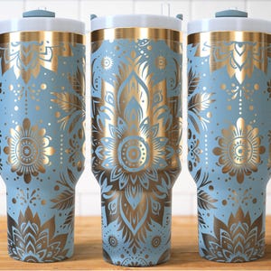 May include: Three light blue insulated tumblers with gold floral patterns. Each has a white lid, a blue handle, and a gold band. The floral design includes flowers, leaves, and other decorative elements.