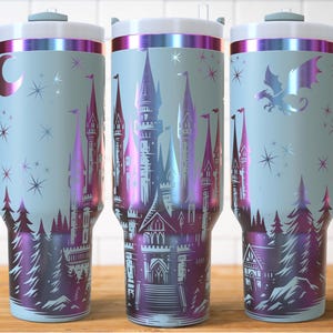 Puede incluir: Tres vasos aislados de color azul claro con un dise&ntilde;o de castillo de fantas&iacute;a. El dise&ntilde;o presenta un castillo, &aacute;rboles, estrellas y un drag&oacute;n en tonos morados y rosas. Cada vaso tiene un asa y una tapa blanca con borde plateado.