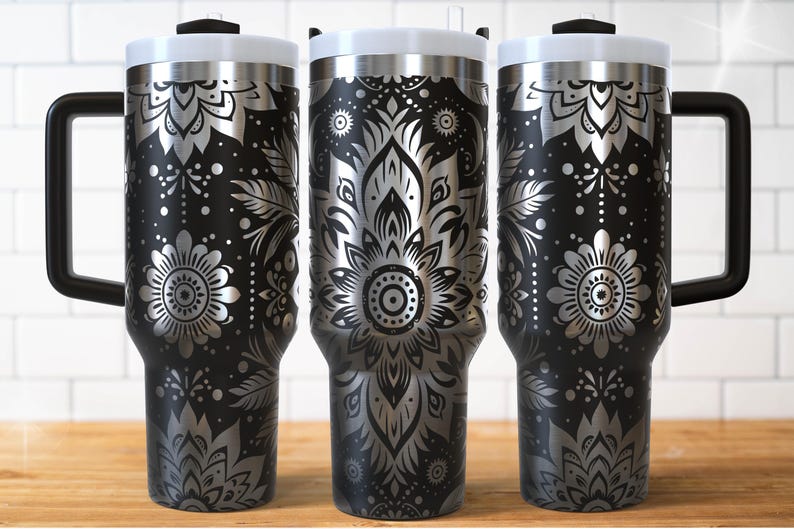 May include: Three black insulated travel mugs with silver floral patterns. Each mug has a white lid, a black handle, and a black rim. The floral design includes flowers, leaves, and dots. The mugs are on a wooden surface.